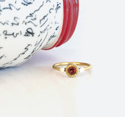 A gold-colored brass ring with a star-burst bezel setting containing a red garnet gem.