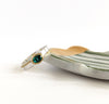 a blue-green quartz.&nbsp;
This oval quartz has been carefully set in a crimped brass bezel. Then a clever raised line of brass hugs the top of the silver band but then drops down to the bottom on its journey around the band.